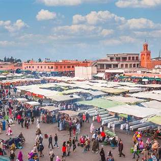 Aerial view of Jemaa el-Fnaa square in Marrakech filled with people and market stalls under a blue sky.