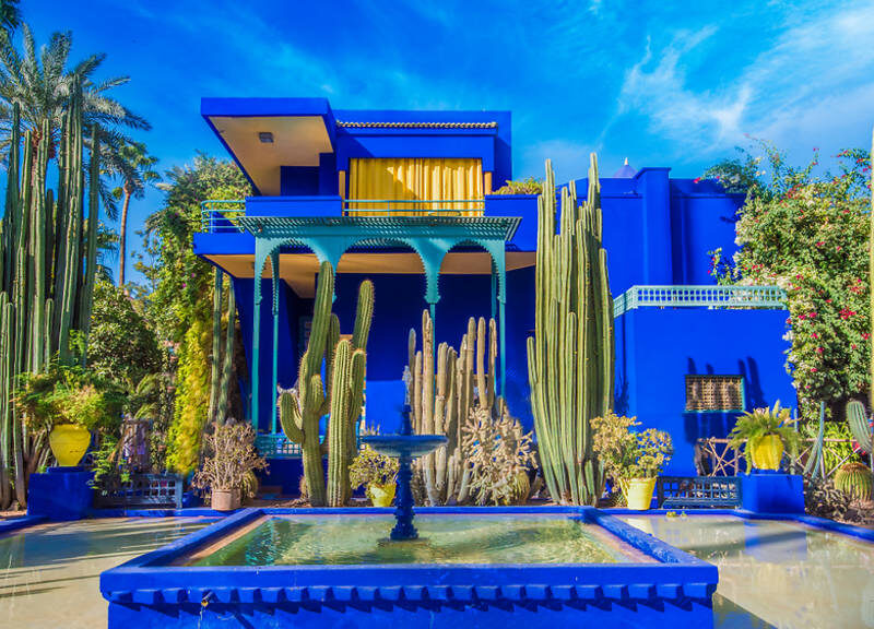 Bright blue and yellow pavilion in Majorelle Garden surrounded by lush plants in Marrakech