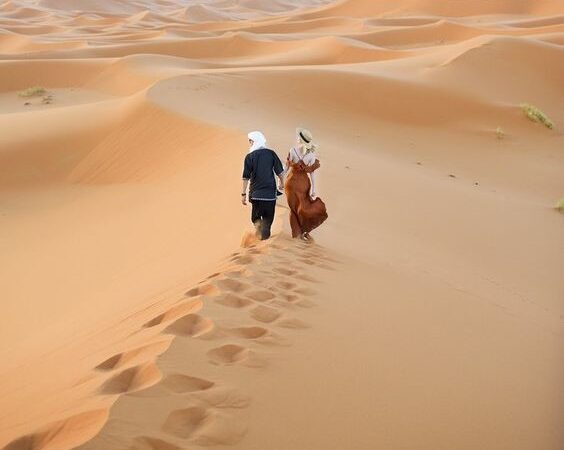 Couple walking hand-in-hand through the golden Sahara Desert dunes during a Morocco honeymoon tour