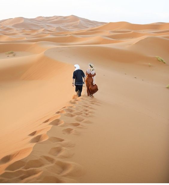 Couple walking hand-in-hand through the golden Sahara Desert dunes during a Morocco honeymoon tour