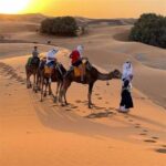 Camel trek in the Moroccan desert with travelers at sunset