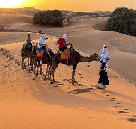 Camel trek in the Moroccan desert with travelers at sunset